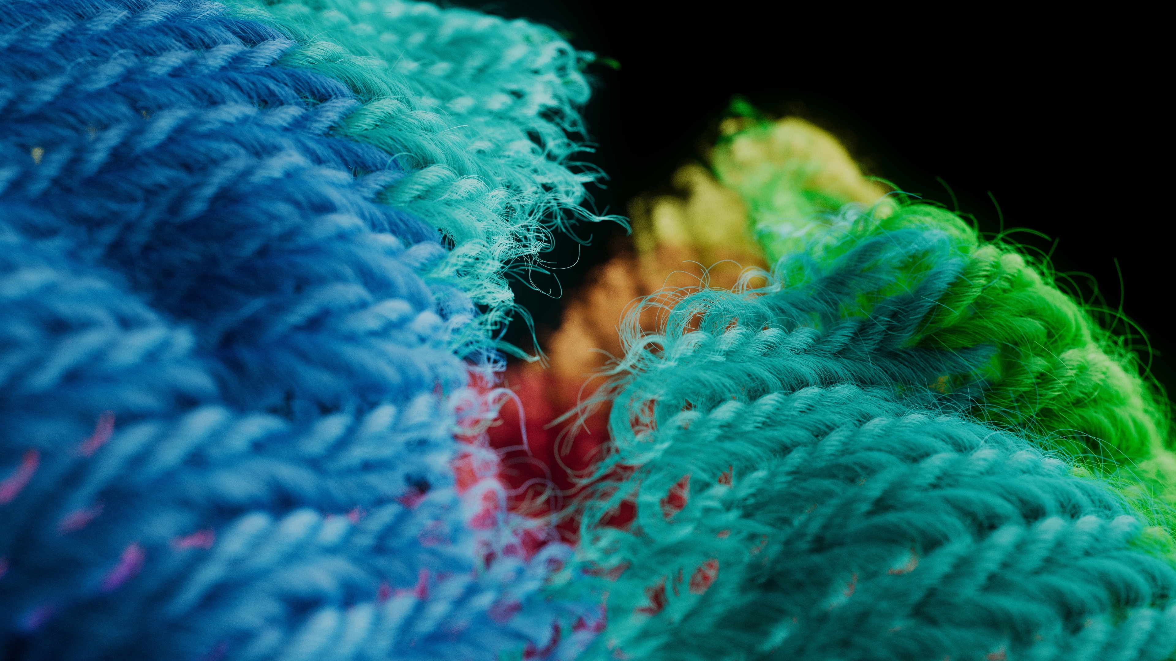 Close-up of blue, teal and green knitted yarn with fuzzy fibers, a red and yellow seam glowing between the folds